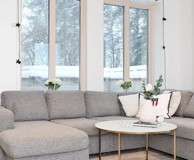 Ljust vardagsrum med grå hörnsoffa, stora fönster och ny takpanel.