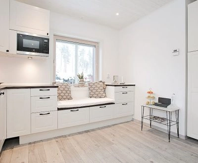 Modernt kök med vit inredning, inbyggd sittbänk och stora fönster.