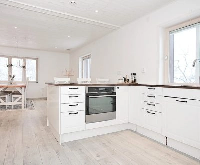 Kök med vit köksinredning, köksö och nya golv, sett från matsalsdelen.