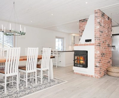 Matplats med vitmålat tak, träbord och stolar bredvid tegelklädd braskamin.